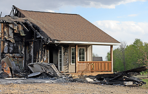 Burned house exterior showing severe fire damage and partial destruction.
