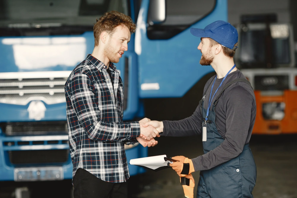 Mechanic and client shaking hands in front of blue truck with clipboard.