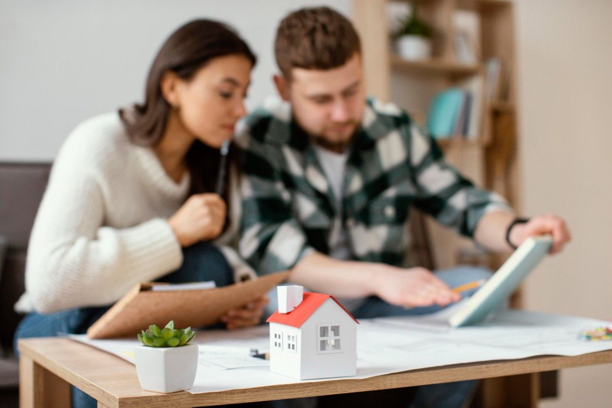 Couple reviewing documents at home with small house model on table.